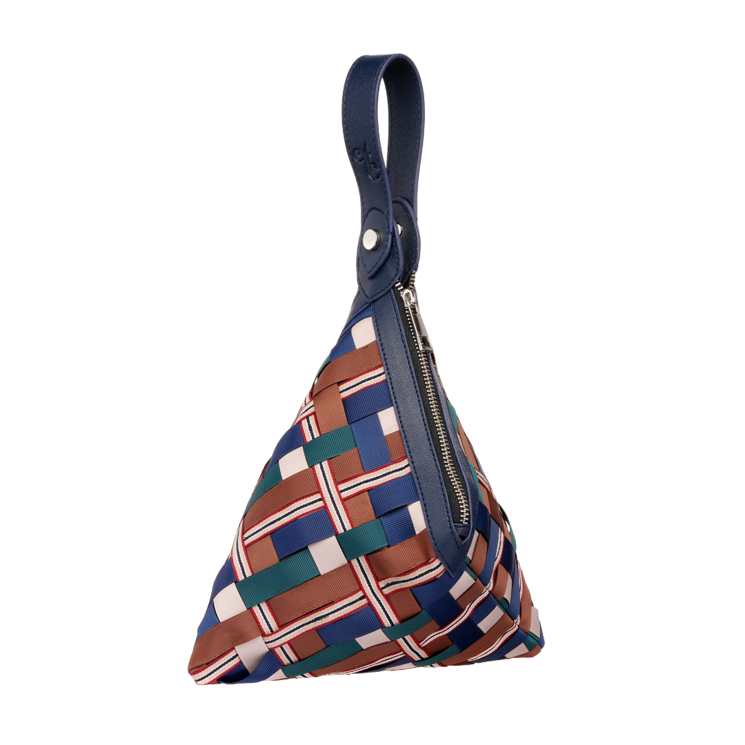 Woman in polka dot dress showcasing a multicolor woven wristlet with navy handle and zip closure from Etcetera.